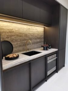 Sleek black kitchen with a marble countertop, brass faucet, and built-in oven; cookies on a plate near the sink.