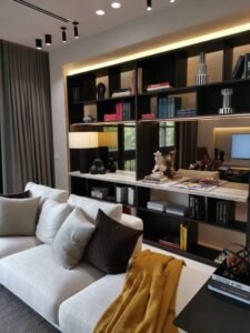 Modern living room with a dark wood built-in bookshelf behind a white sofa, gray and brown cushions, and a mustard throw blanket.
