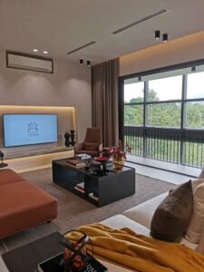 Modern living room with a wall-mounted TV, brown armchairs, and a black coffee table facing a large window with greenery outside.