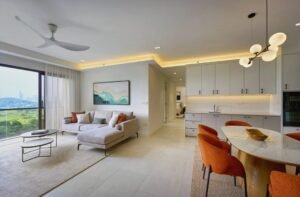 Open-plan living room and kitchen: beige sectional sofa, two round coffee tables, marble dining table with orange chairs, and a city/green view through large windows.