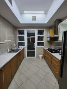 Bright galley kitchen with wooden cabinets, granite counters, left sink, right gas range, fridge, and a skylight above the ceiling.