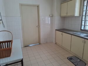 A small kitchen with white tiled walls and floor, beige cabinets, a stainless sink by a window, and a doorway in the center. A table with a wicker basket is on the left.