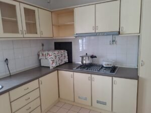 Cream kitchen with upper and lower cabinets, white tiled backsplash, and a gas stove with a pot on the burner.