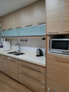 Modern kitchen with wooden cabinets, a double sink, kettle, and microwave on a white countertop.