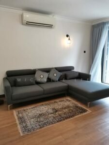 A modern L-shaped gray sectional sofa on a light wood floor, with a patterned rug, a wall lamp, and a window with sheer curtains in a bright living room.