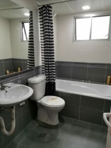 Small bathroom with a white sink, toilet, and bathtub, a striped black-and-white shower curtain, and grey tiled walls.