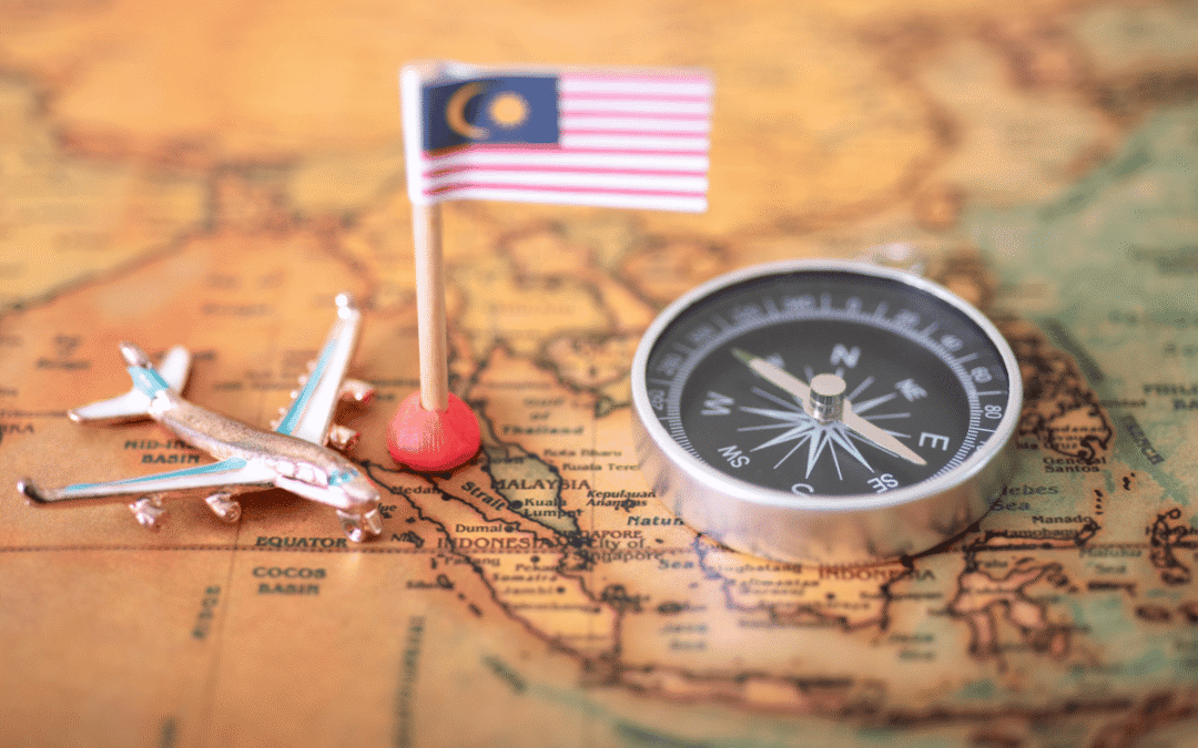 Miniature Malaysian flag on a pin, a small toy airplane, and a compass resting on a vintage map—travel theme.
