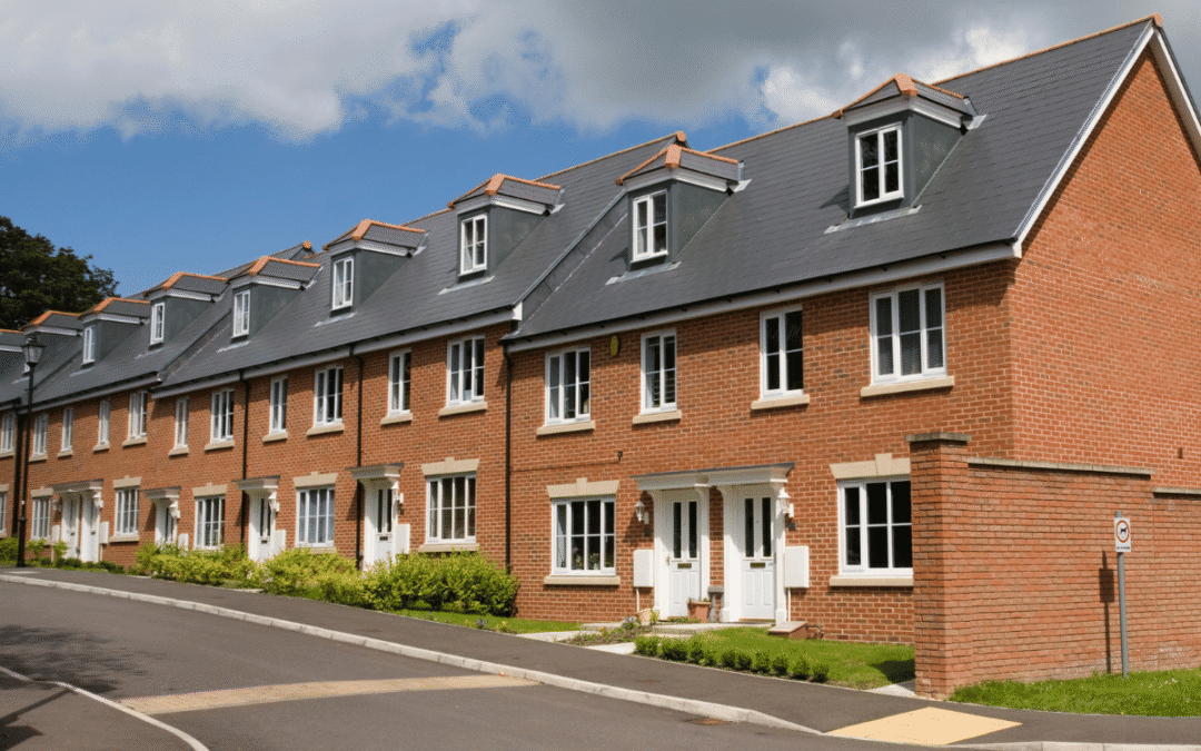 Row of red brick townhouses with white doors and dormer windows along a curved street.