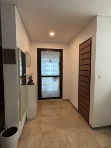 Hallway with beige tile floor, glass door at end, wooden panel door on the right, and a potted plant on the left.