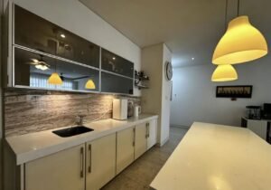 Modern kitchen with white cabinets, marble backsplash, and a long island under yellow pendant lights.