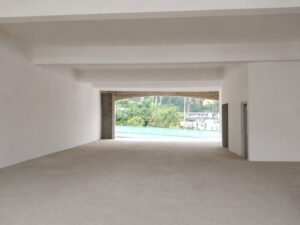 Empty white-walled hall with a wide open doorway at the far end, revealing a green outdoor area and trees beyond.