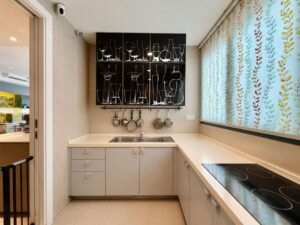 Compact modern kitchen with light gray cabinetry, a double sink, and an induction cooktop along a white countertop; pots hang under a black cabinet above the sink.