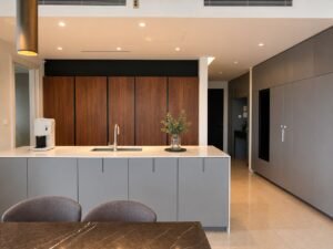 Modern kitchen with a gray island, stainless sink, and a wood-paneled wall backdrop with a large refrigerator on the right.