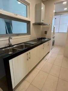 Modern kitchen with white cabinets, black countertop, double sink, and a gas cooktop under a stainless range hood.