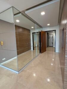 Modern interior hallway with glass partition and mirrored panels, wood-paneled walls, and a polished tiled floor leading to an open wooden door.