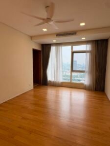 Empty living room with hardwood floor, white walls, and a large window with sheer curtains showing the city skyline outside.
