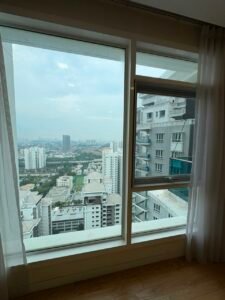 Interior view from a room: sheer white curtains frame a panoramic cityscape of high-rise buildings outside on a sunny day.