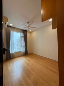 Empty modern bedroom with large window, sheer gray curtains, light wood floor, ceiling fan, and built-in wooden wardrobe on the right.