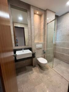 Modern bathroom with a wall-mounted sink, large mirror, and glass-enclosed shower on beige stone walls.