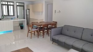 Open-plan living area with a gray sofa, wooden dining table and six chairs, and a white modern kitchen in the background.
