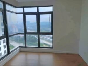 Empty corner room with large black-framed bay windows and a cityscape view over a river; light wood floor.