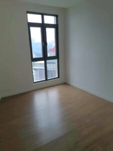 Empty empty room with a tall window letting in daylight; light wood floor and white walls, minimal space.