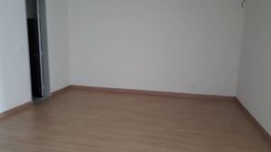 Empty, unfurnished room with light wood laminate flooring and white walls; door slightly open on the left side of the image.