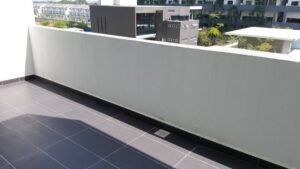 Balcony with dark gray tiled floor and a white parapet, overlooking modern residential buildings and trees.