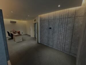 Modern office reception with marble-panel wall on the right, a desk and black chair to the left, and a glass door at the far end.