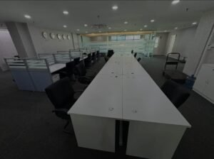Empty open-plan office with a long white desk, black chairs, and glass partitions across the room