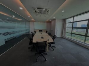 Modern conference room with a long oval table, black chairs, glass walls, and a city view through large windows.