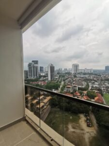 Balcony with glass railing overlooking a city skyline of high-rise buildings on a cloudy day.