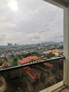 Balcony view of a city: red-roofed buildings in the foreground, a parking lot, and a construction site to the right under a cloudy sky.