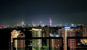 Night city skyline at night with illuminated high-r rises seen from a balcony railing.