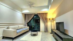 Modern living room with a beige sofa, a round black coffee table, and a low TV stand beside a floor lamp. Curtains frame a balcony door in the background.