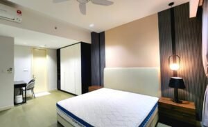 Modern hotel room with a large bed, two wooden nightstands, and pendant lamp against a beige accent wall and striped paneling.